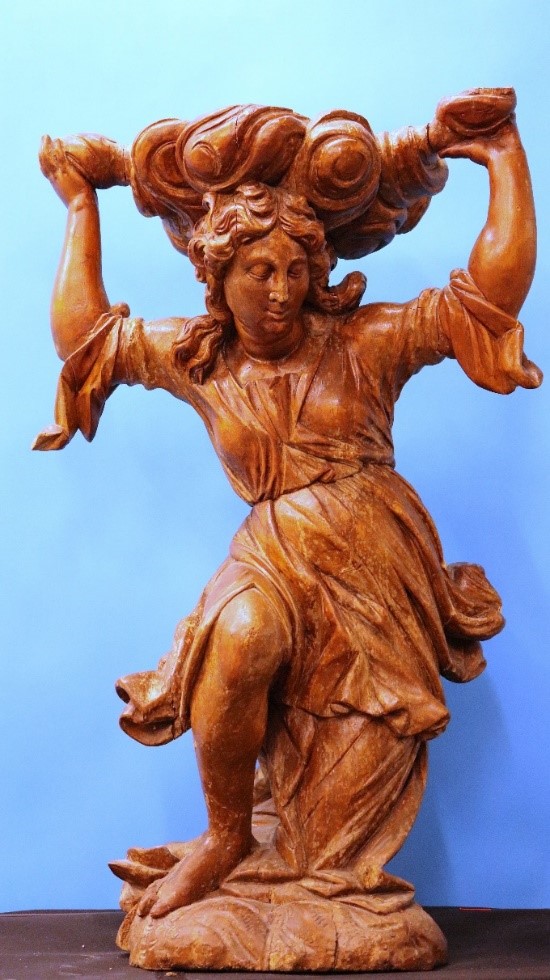 Eine hölzerne weibliche Figur mit welligem Haar erhebt vor einem hellblauen Hintergrund die Arme über den Kopf, auf dem ein wolkenähnliches Gebilde ruht. (verweist auf: Holzengel ziert künftig wieder tschechische Kirche)